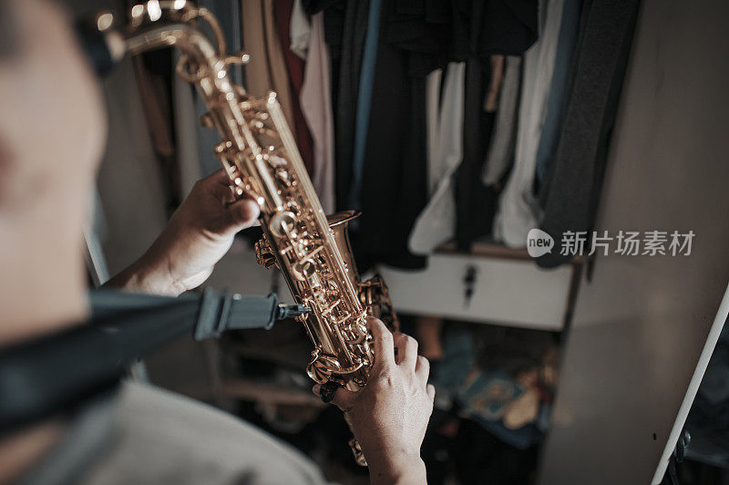 asian chinese mid adult man practicing saxophone facing his wardrobe as soundproof to reduce the sounds disturbing his neighbor  in his apartment